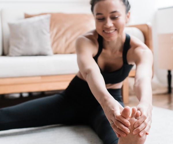 Smiling woman stretching gently on a yoga mat in a sunlit room.